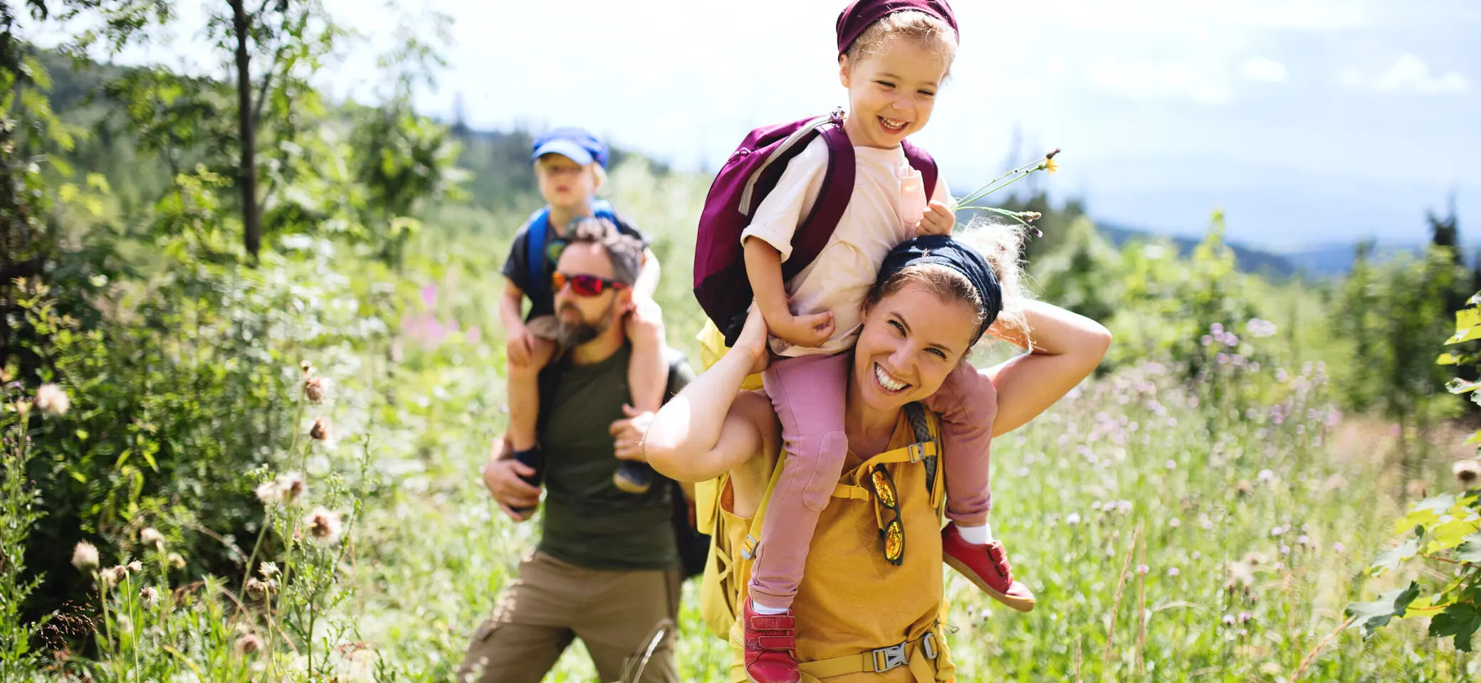 Eine Familie in der Natur, die Mutter trägt ein Kind auf den Schultern | © Halfpoint / Adobe Stock